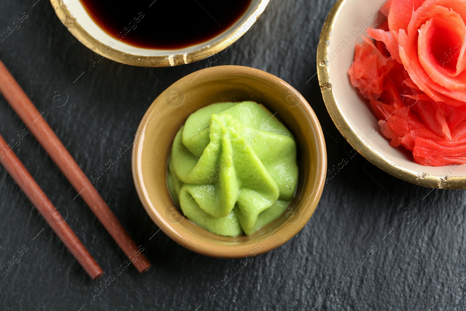 Photo of Hot wasabi paste, soy sauce, ginger and chopsticks on dark textured table, flat lay