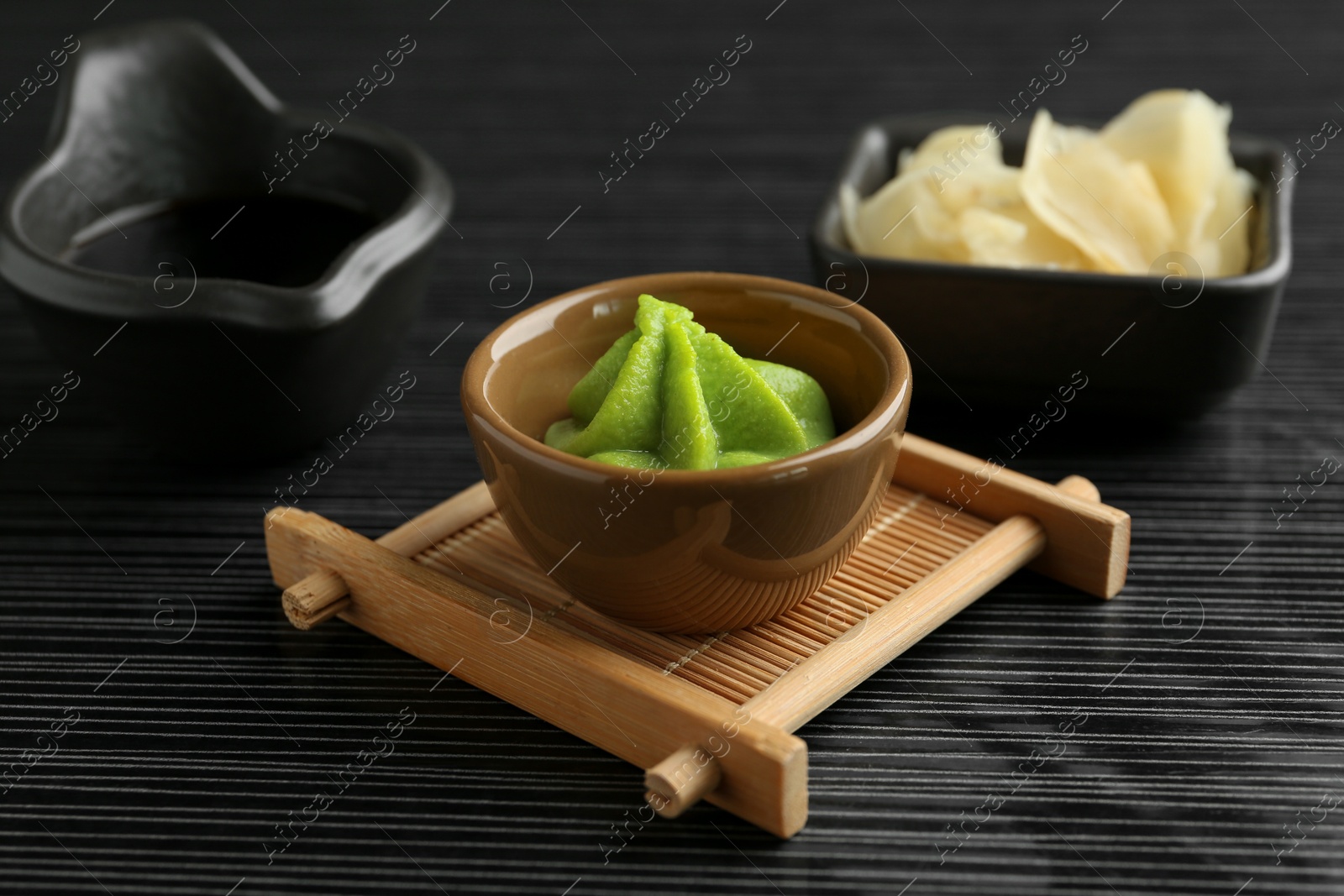 Photo of Hot wasabi paste, soy sauce and ginger on black textured table, closeup