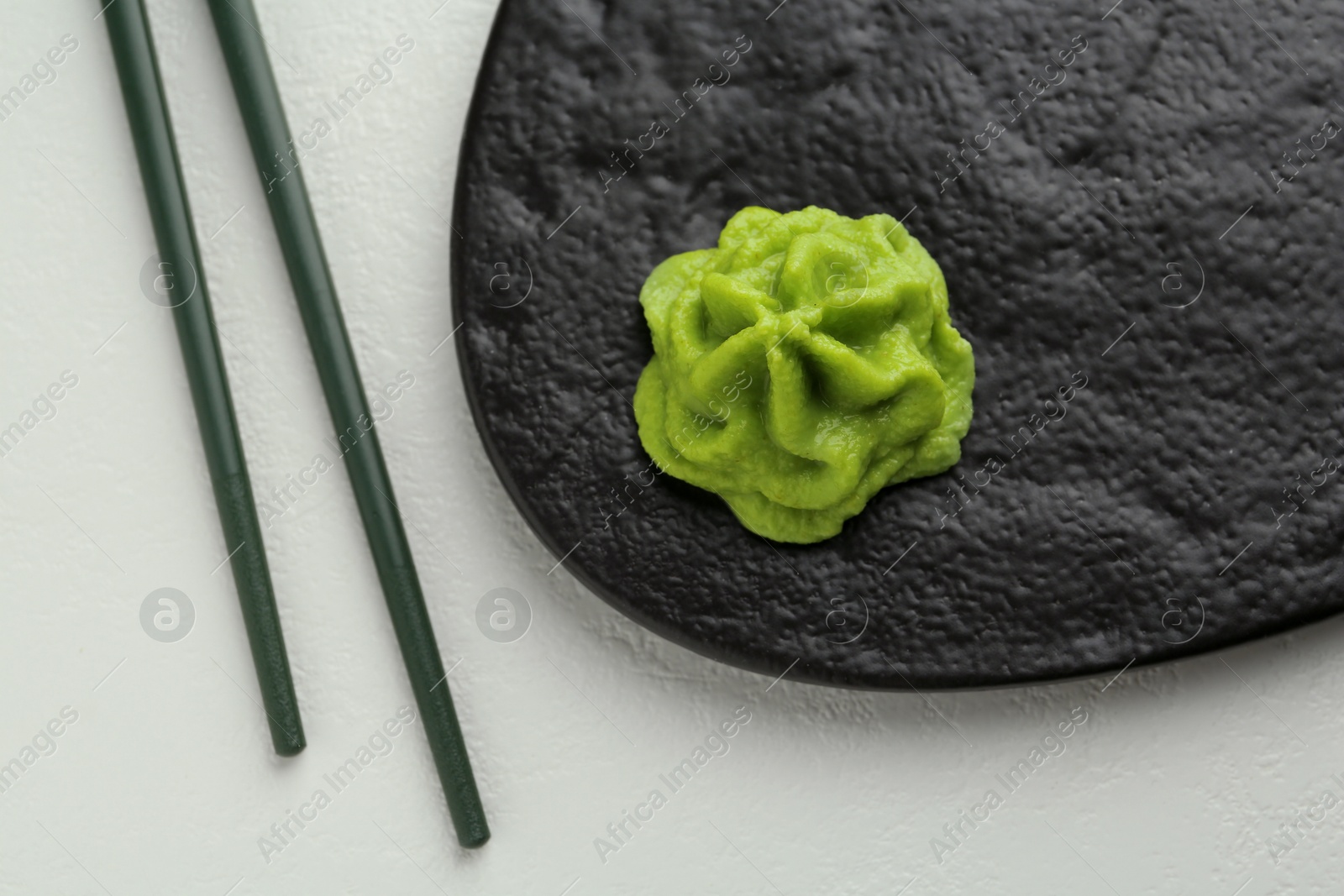 Photo of Slate board with hot wasabi paste and chopsticks on light textured table, top view