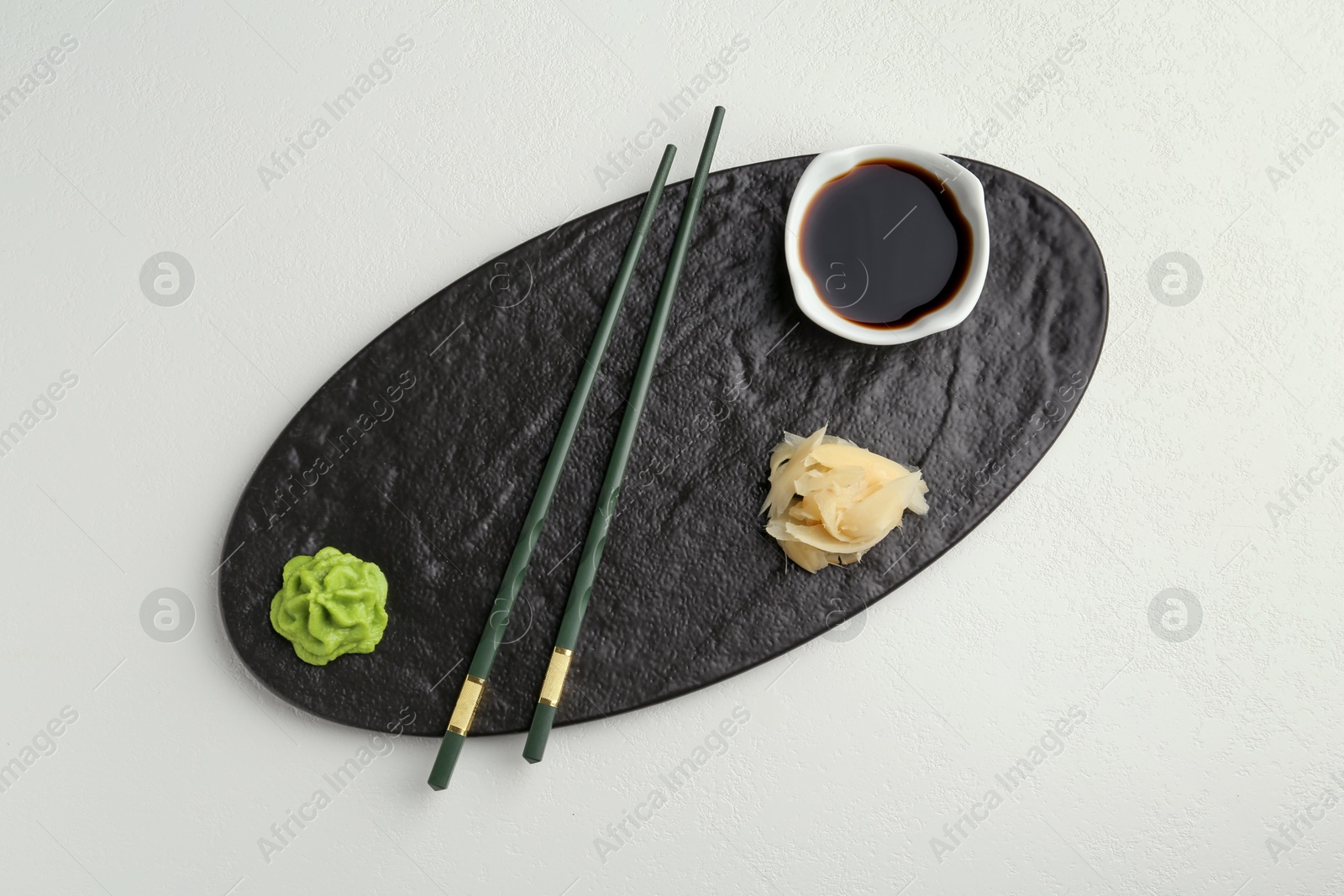 Photo of Hot wasabi paste, soy sauce, ginger and chopsticks on light textured table, top view