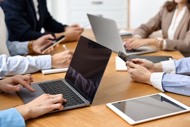 Photo of Group of people using different gadgets at wooden table in office, closeup. Modern technology