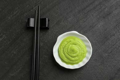 Photo of Hot wasabi paste and chopsticks on dark textured table, top view