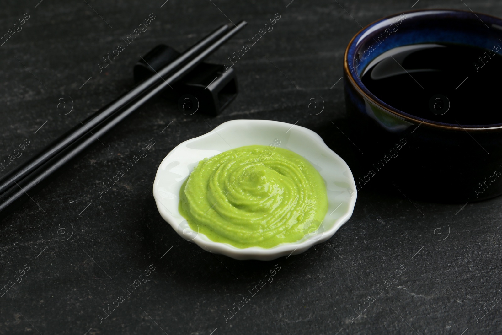 Photo of Hot wasabi paste, soy sauce and chopsticks on dark textured table, closeup