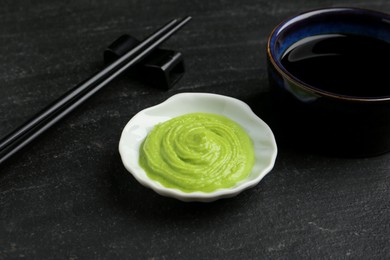 Photo of Hot wasabi paste, soy sauce and chopsticks on dark textured table, closeup