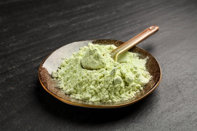 Photo of Plate with dry wasabi powder and spoon on dark textured table, closeup