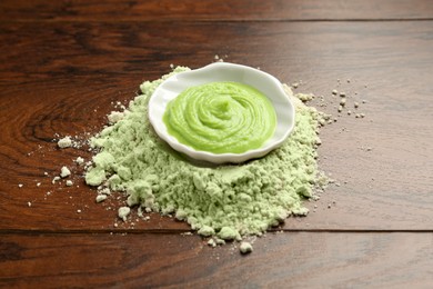 Photo of Pile of dry wasabi powder and bowl with paste on wooden table, closeup