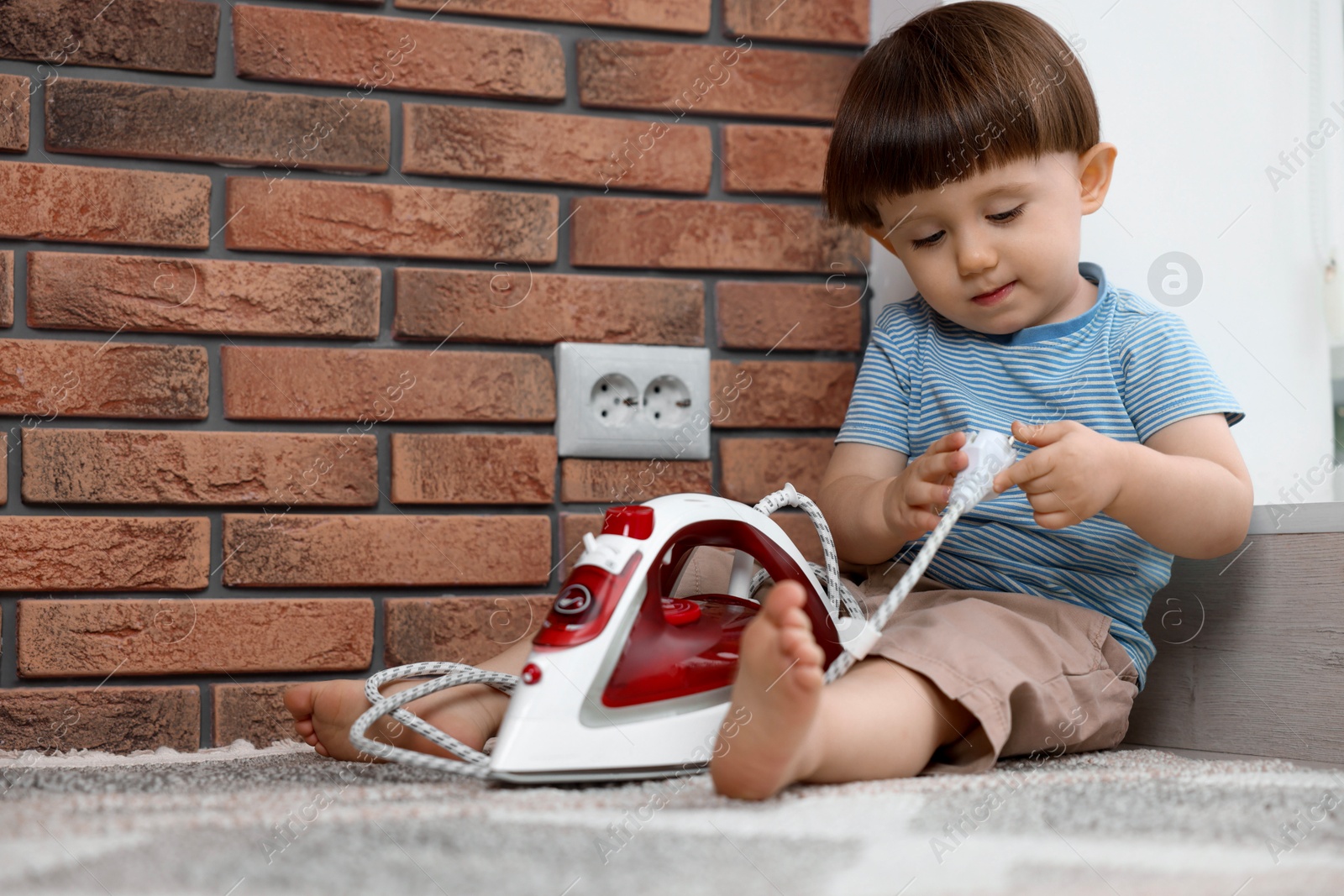 Photo of Little boy playing with iron plug near electrical socket at home. Child in danger