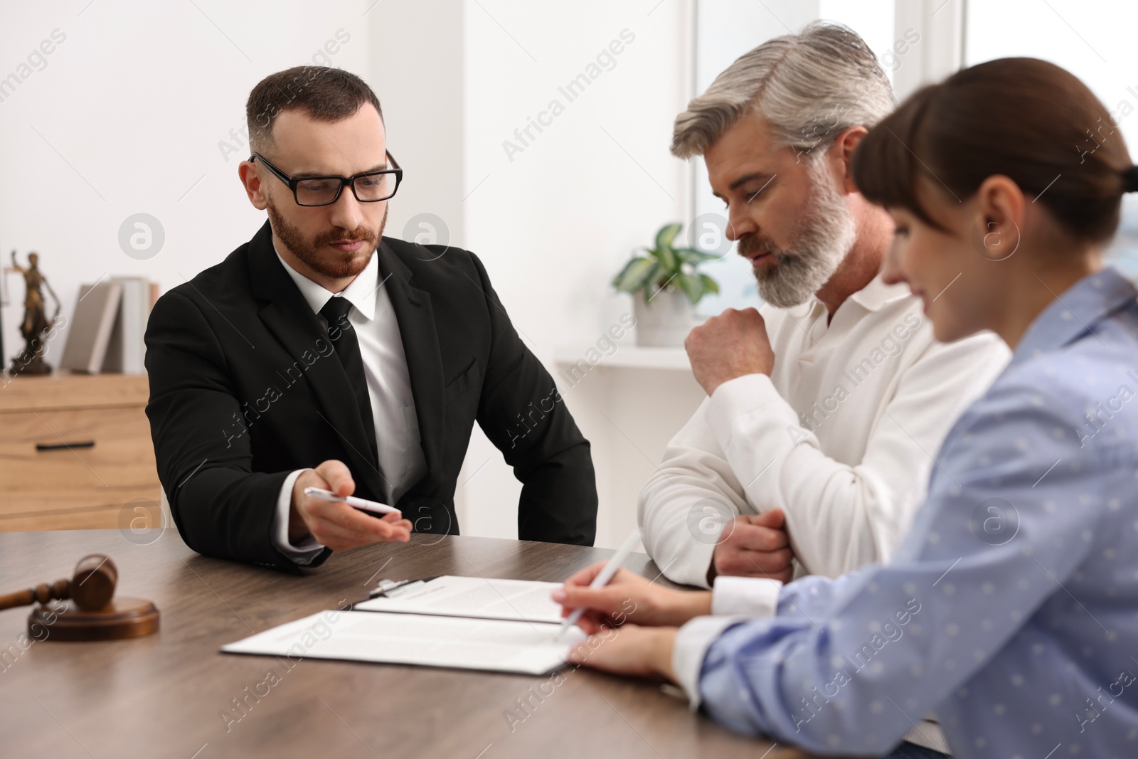 Photo of Couple having meeting with professional notary at wooden desk indoors