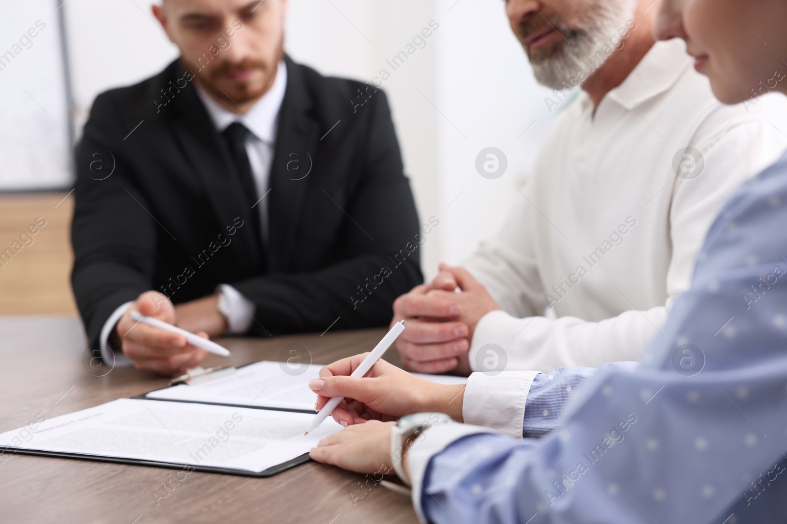 Photo of Clients signing notarial paperwork during meeting with lawyer at wooden desk indoors, closeup