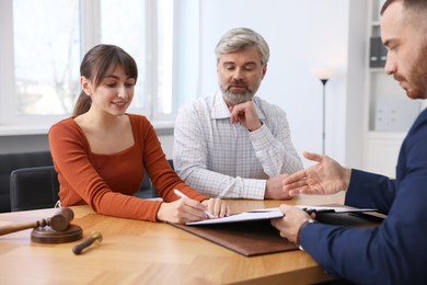 Photo of Clients signing notarial paperwork during meeting with lawyer at wooden desk indoors