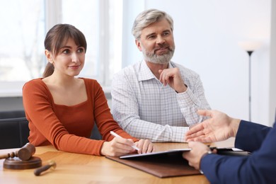 Photo of Clients signing notarial paperwork during meeting with lawyer at wooden desk indoors