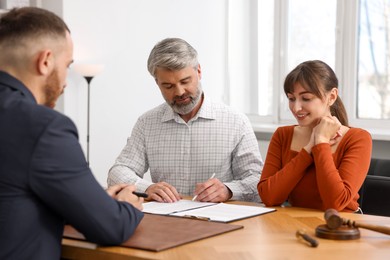 Clients signing notarial paperwork during meeting with lawyer at wooden desk indoors