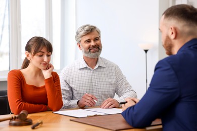 Photo of Clients signing notarial paperwork during meeting with lawyer at wooden desk indoors