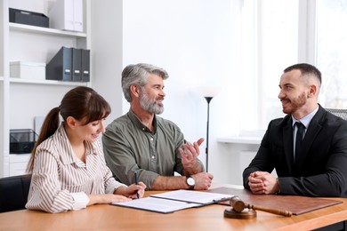 Photo of Clients signing notarial paperwork during meeting with lawyer at wooden desk indoors