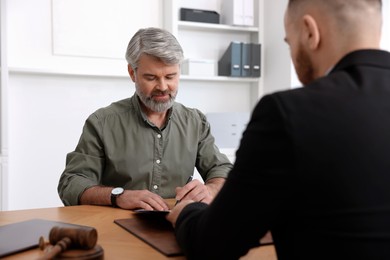 Photo of Client signing notarial paperwork during meeting with lawyer at wooden desk indoors