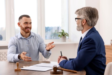 Man having meeting with professional lawyer at wooden desk indoors