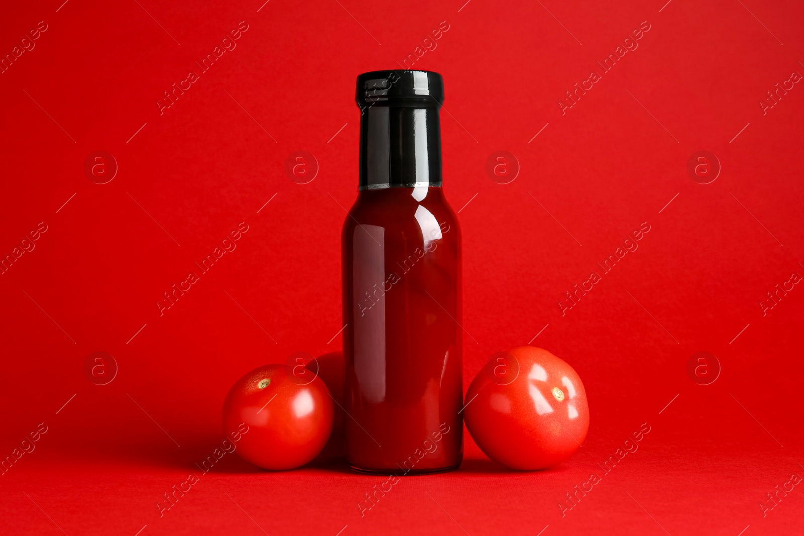 Photo of Ketchup in glass bottle and fresh tomatoes on red background