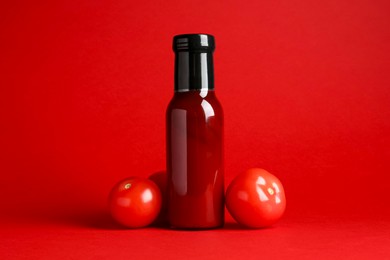 Photo of Ketchup in glass bottle and fresh tomatoes on red background