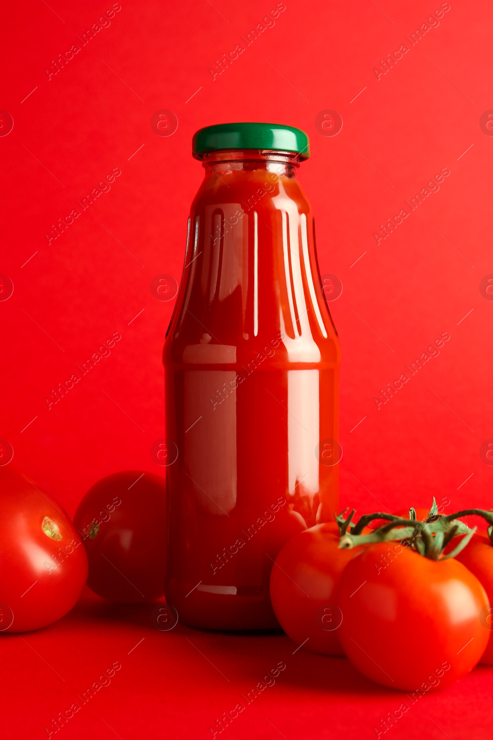 Photo of Ketchup in glass bottle and fresh tomatoes on red background