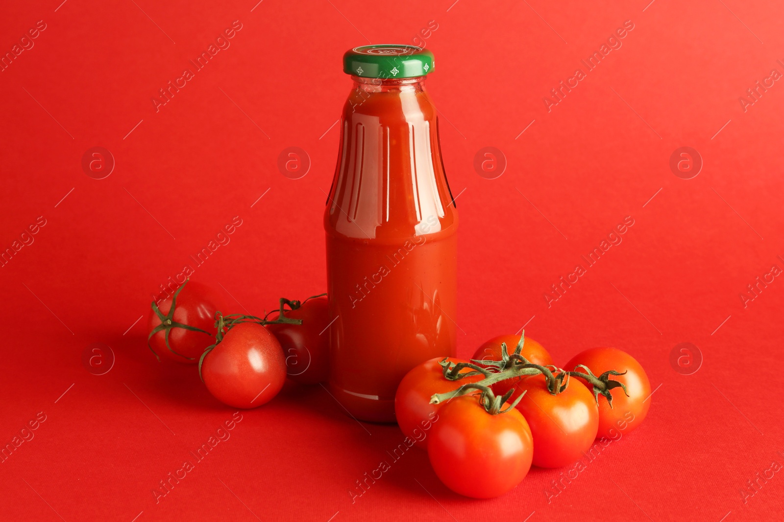 Photo of Ketchup in glass bottle and fresh tomatoes on red background