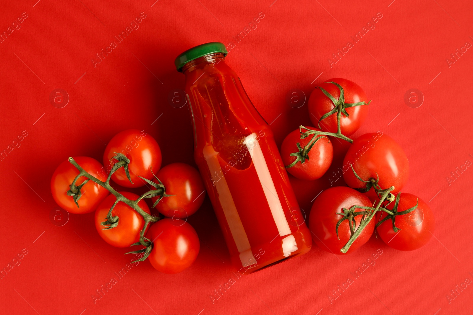 Photo of Ketchup in glass bottle and fresh tomatoes on red background, top view