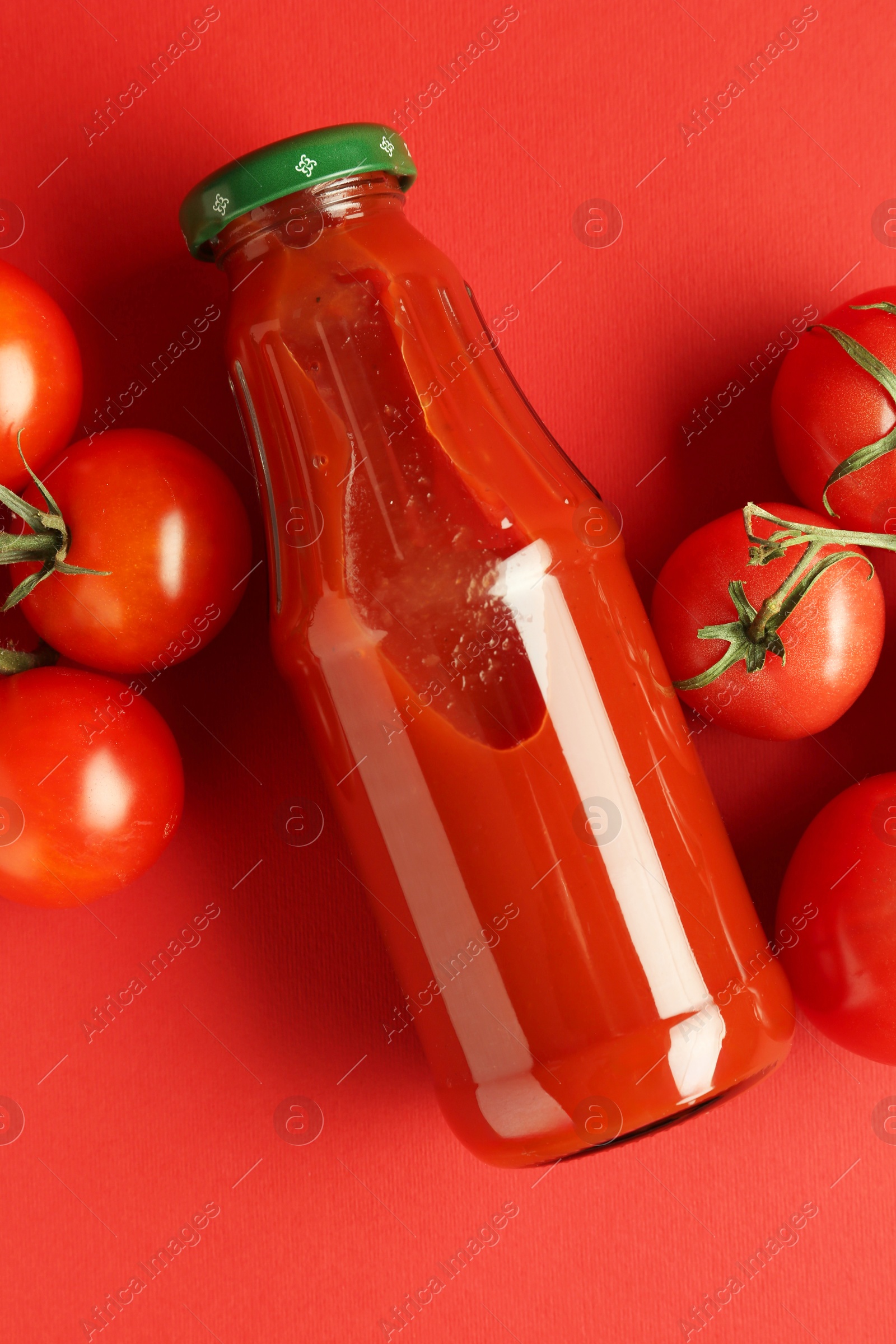 Photo of Ketchup in glass bottle and fresh tomatoes on red background, top view