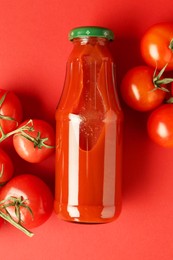 Photo of Ketchup in glass bottle and fresh tomatoes on red background, top view