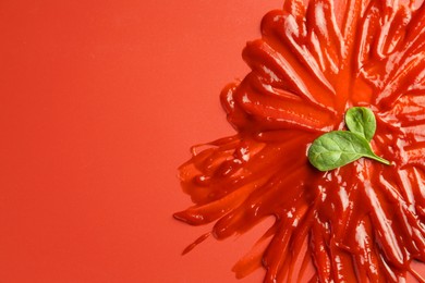 Photo of Tasty ketchup and basil on red background, top view. Space for text