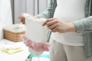 Photo of Pregnant woman with baby clothes at home, closeup