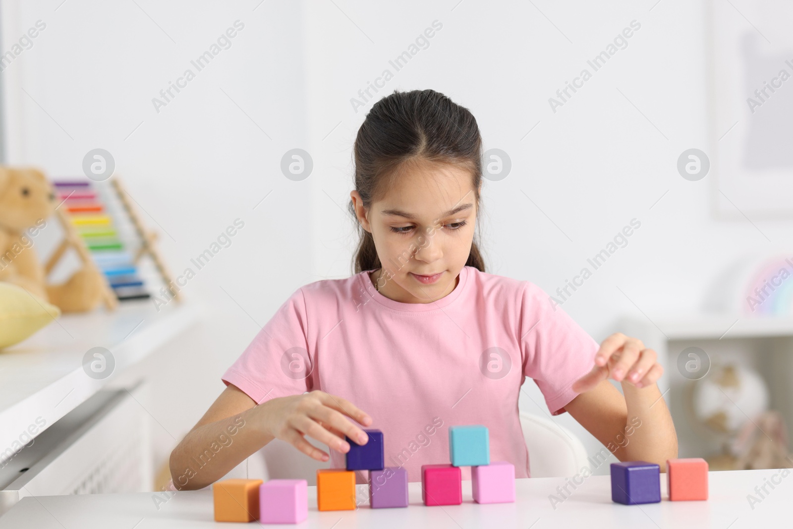 Photo of Girl building pyramid of colorful cubes at table indoors