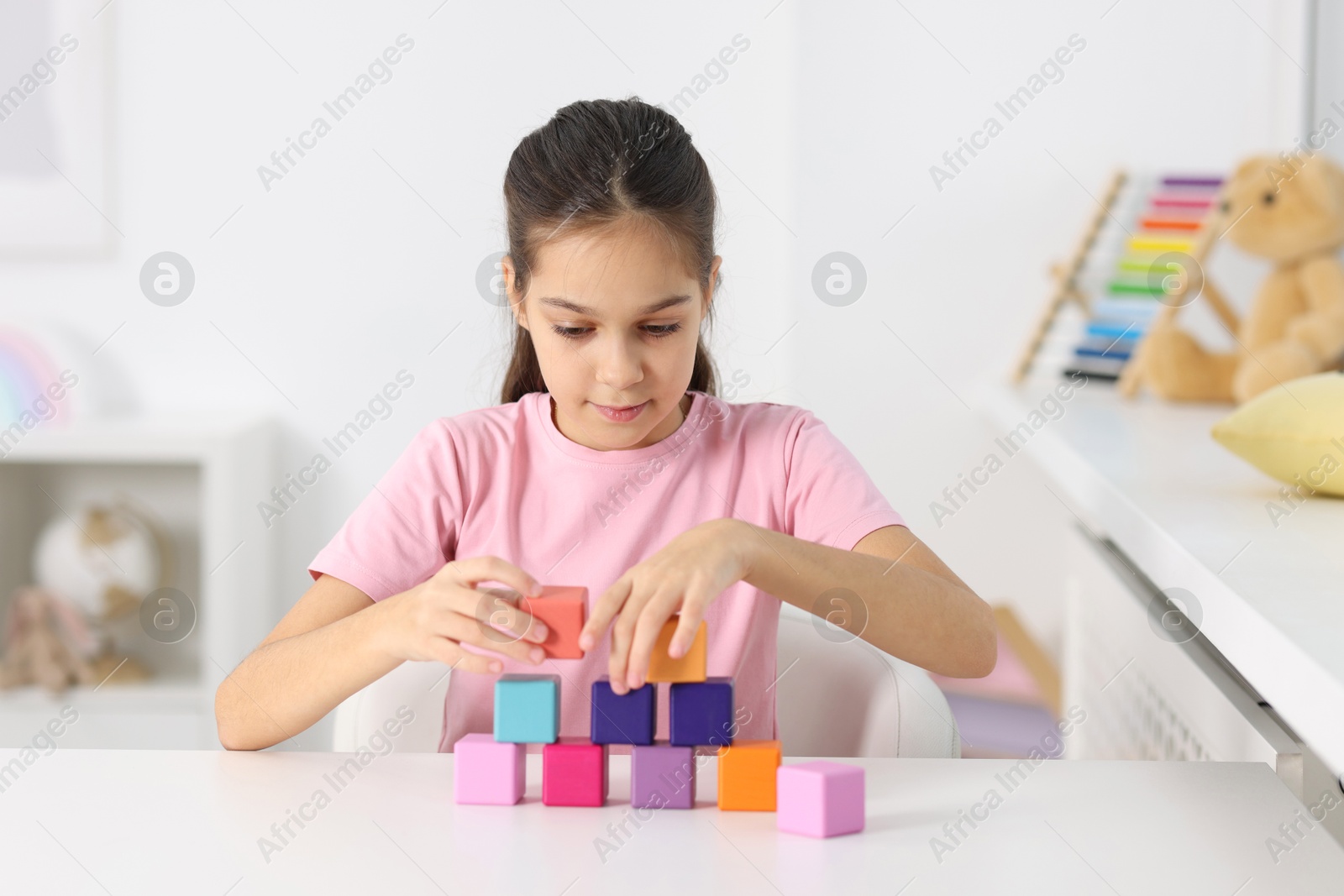 Photo of Girl building pyramid of colorful cubes at table indoors