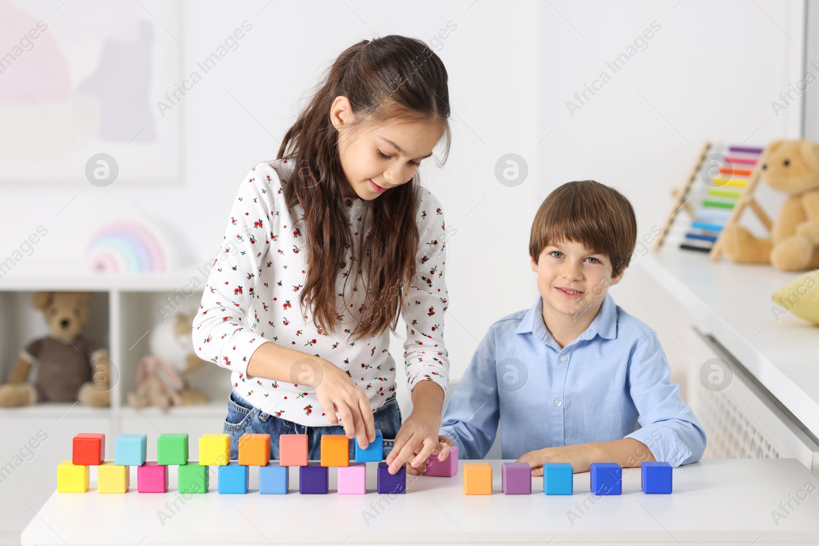 Photo of Children playing with colorful cubes at table indoors