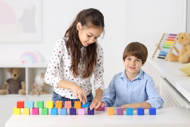 Children playing with colorful cubes at table indoors