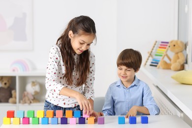 Photo of Children playing with colorful cubes at table indoors