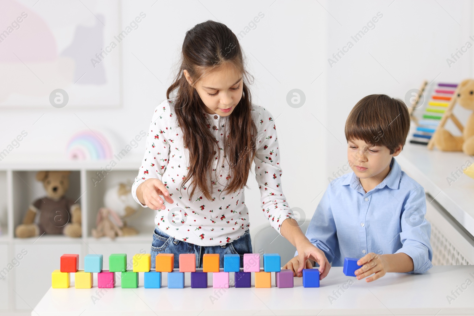 Photo of Children playing with colorful cubes at table indoors