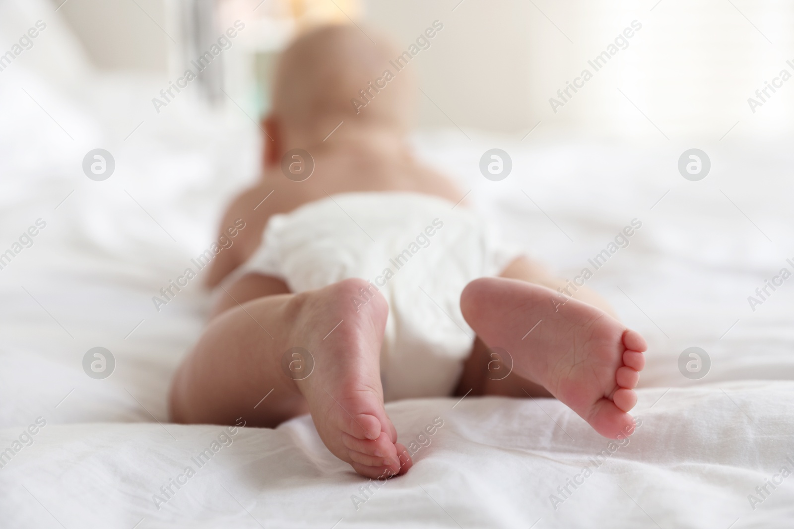 Photo of Cute little baby in diaper on bed indoors, selective focus