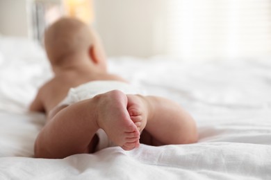 Cute little baby in diaper on bed indoors, selective focus. Space for text