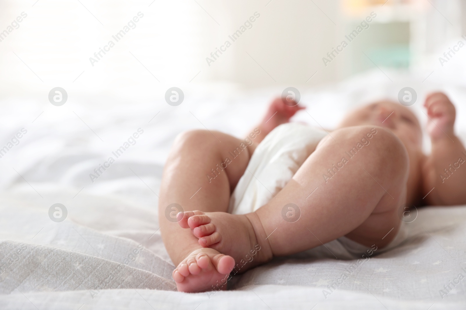 Photo of Cute little baby in diaper on bed indoors, selective focus. Space for text