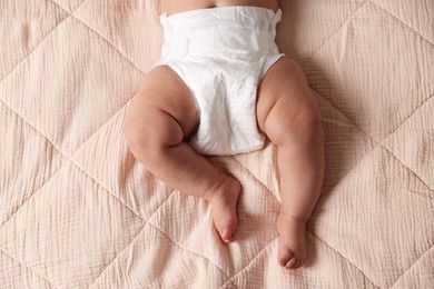 Cute little baby in diaper on bed, top view