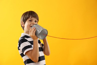 Boy using tin can telephone on yellow background