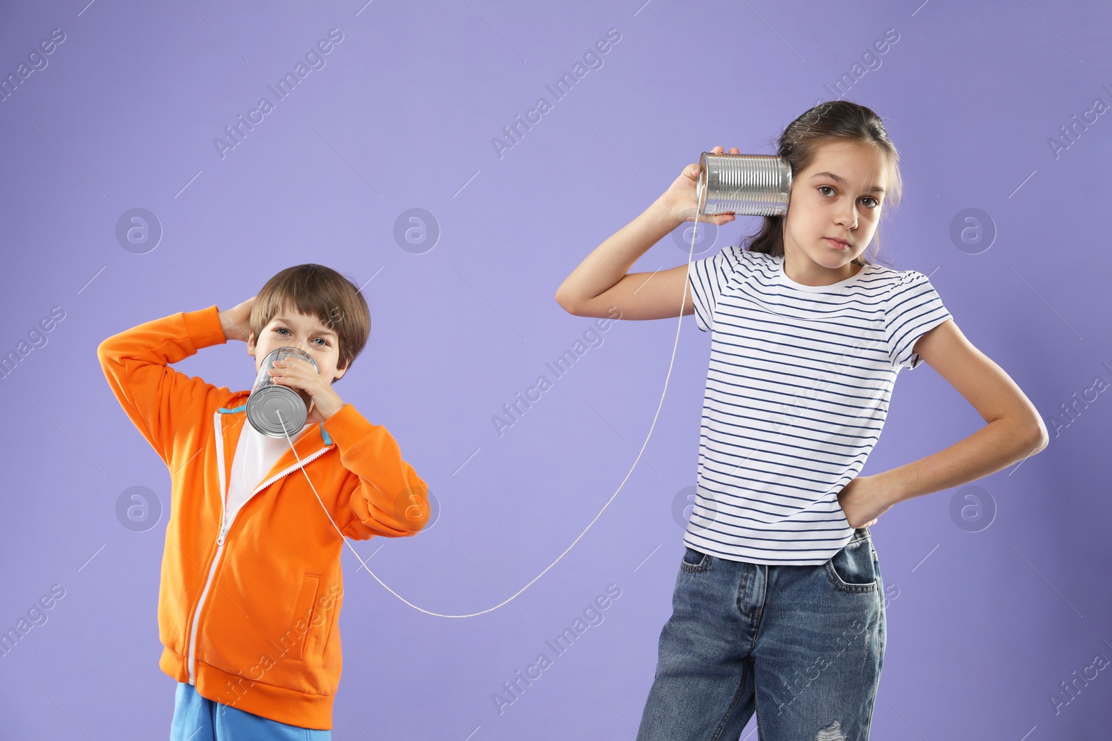 Photo of Girl and boy talking on tin can telephone against violet background