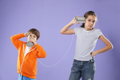 Photo of Girl and boy talking on tin can telephone against violet background