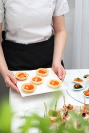 Photo of Woman with many different tasty canapes at white wooden table, closeup