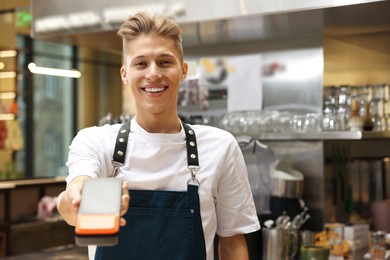 Photo of Smiling cafe worker with payment terminal indoors