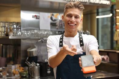 Photo of Smiling cafe worker with payment terminal indoors