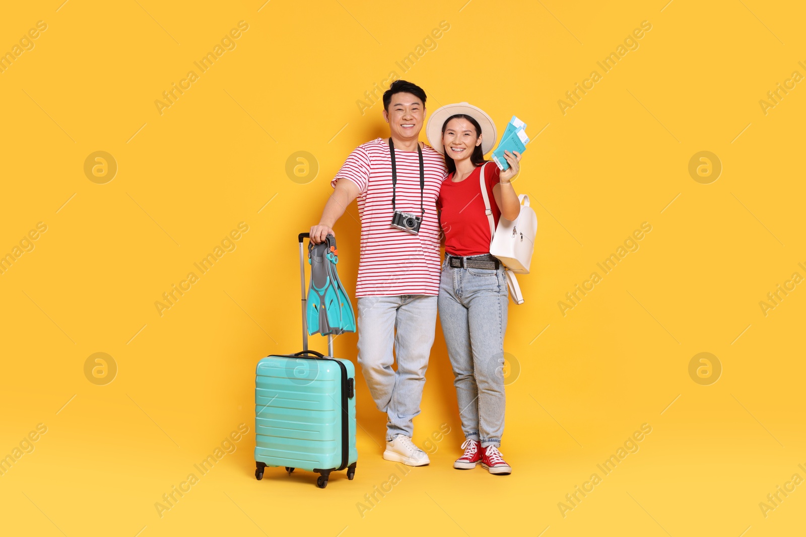 Photo of Happy travellers with passports, swim fins and suitcase on yellow background