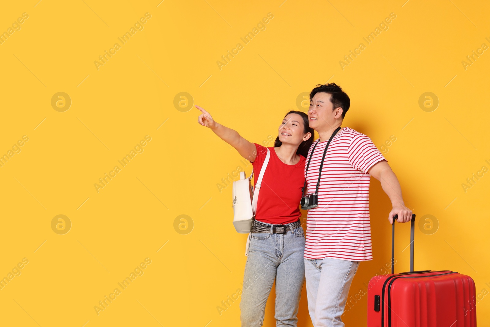 Photo of Happy travellers with suitcase pointing at something on yellow background. Space for text