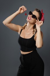 Photo of Happy woman eating cherry on grey background. Pin-up vibes