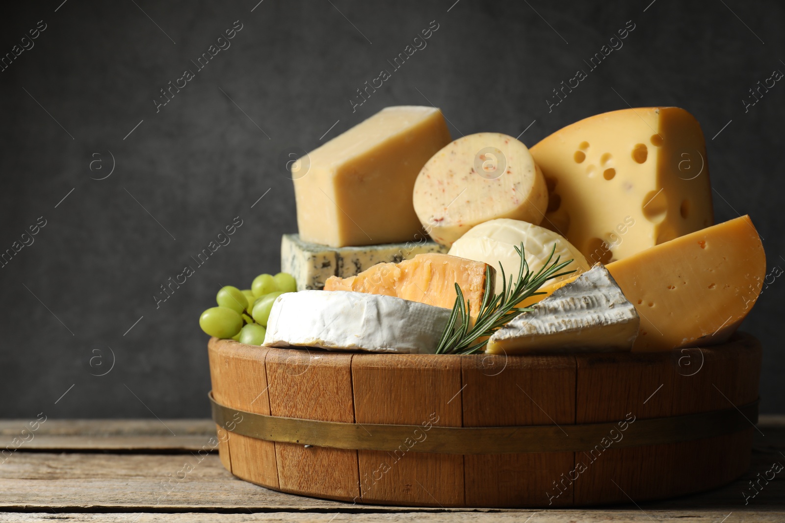 Photo of Different types of cheese, rosemary and grapes on wooden table, space for text