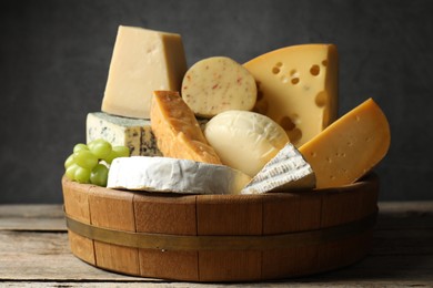 Photo of Different types of cheese and grapes on wooden table, closeup